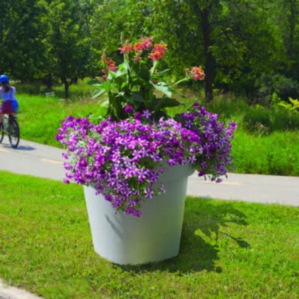 Commercial self-watering planter with purple and pink flowers placed along a park pathway, ideal for low-maintenance streetscape landscaping.